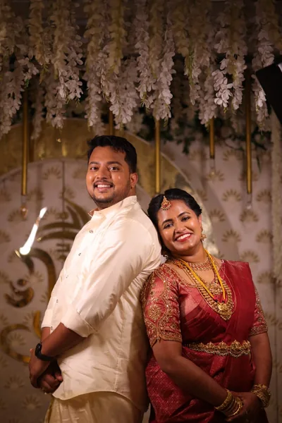 Bride in red silk beside the groom against a floral backdrop