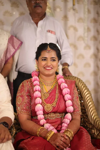 Seated bride in red silk wearing a rose garland